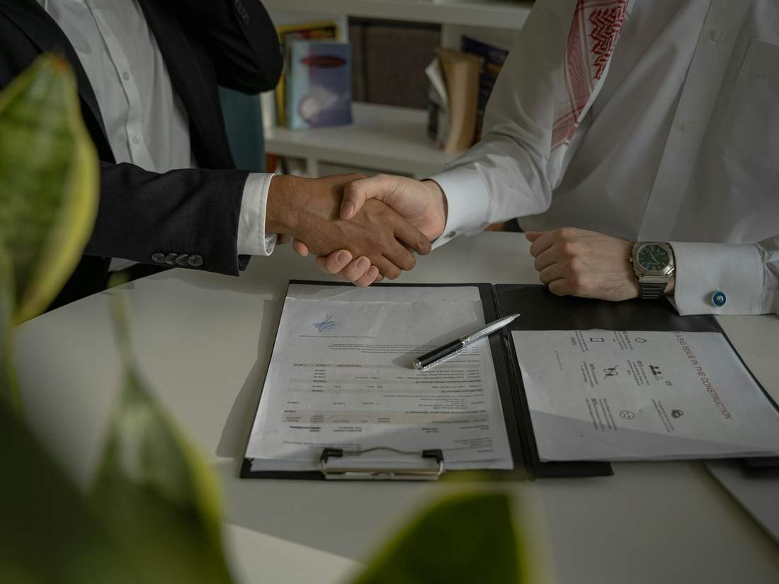 Two people shaking hands over a signed contract on a desk