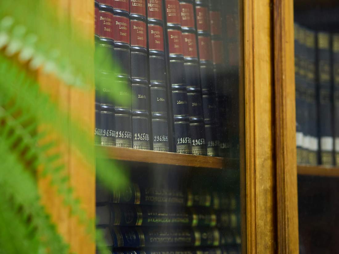 Leather-bound reference volumes on a library shelf behind glass